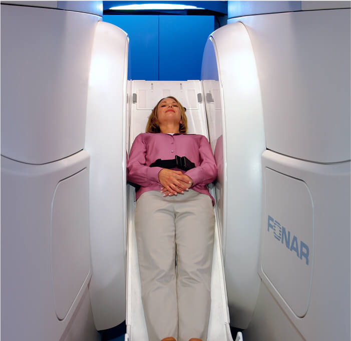 A woman undergoing medical examination or treatment, lying on a machine in a room.